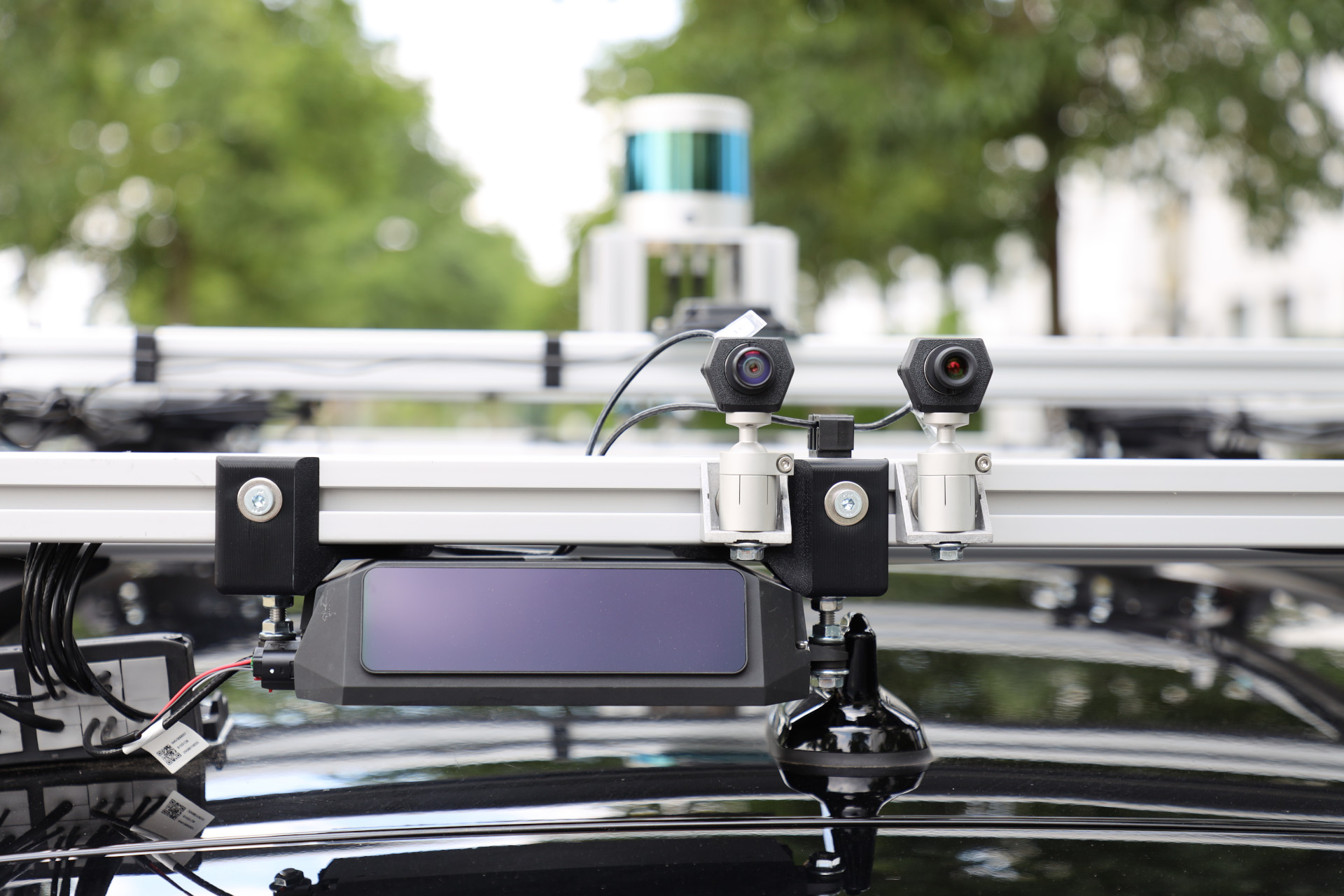 Close-up of two cameras mounted on ball joints on the aluminum roof rack, with a long-range lidar below them and the 360 degree lidar visible in the background.